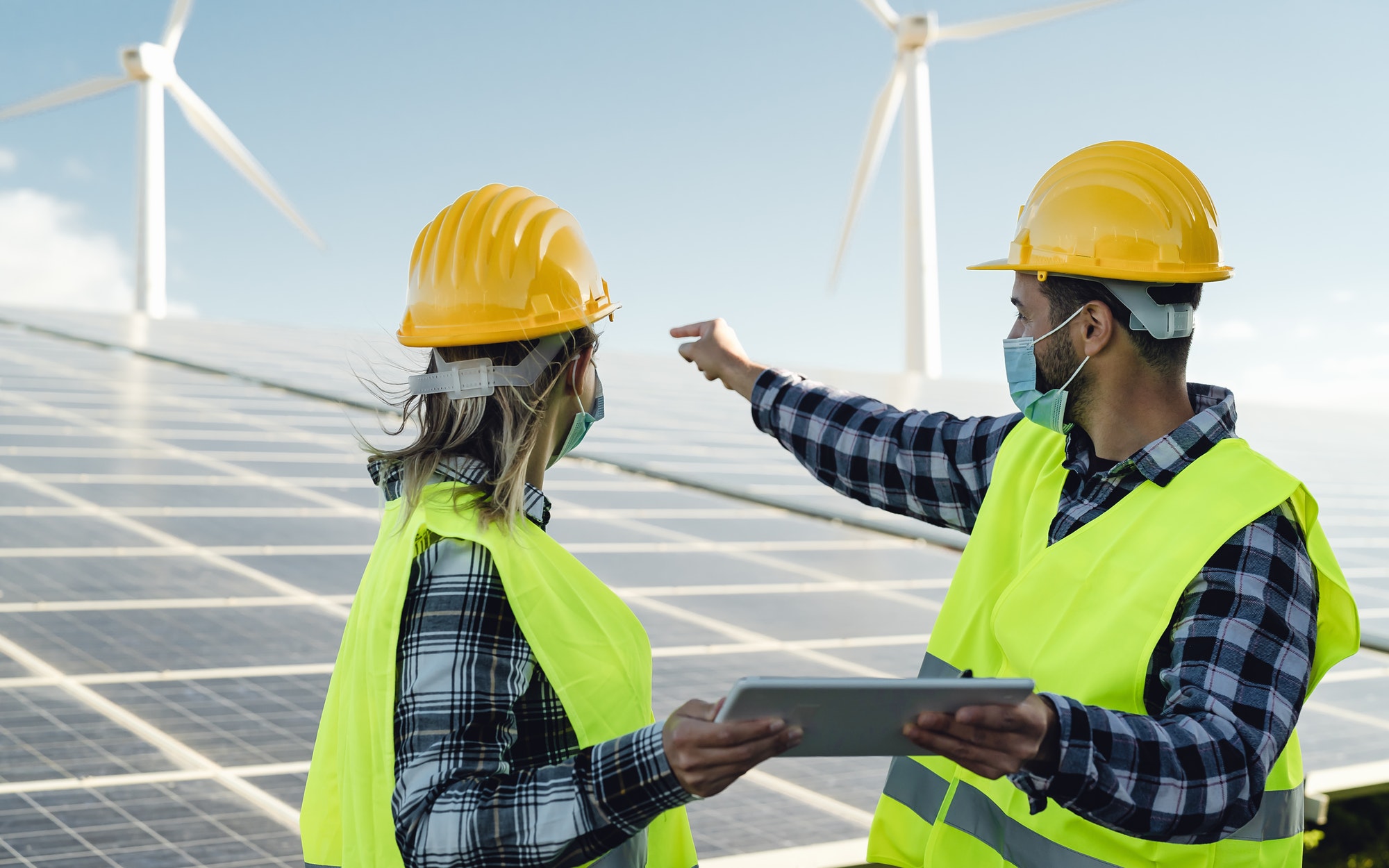 people-working-for-alternative-energy-with-wind-turbine-and-solar-panel-while-wearing-face-mask.jpg